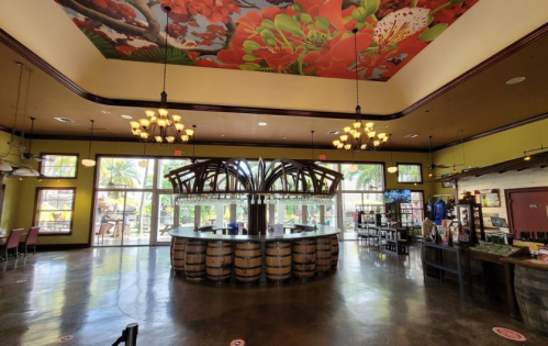 Interior of a vibrant restaurant featuring a large bar made of barrels, colorful ceiling, and large windows.