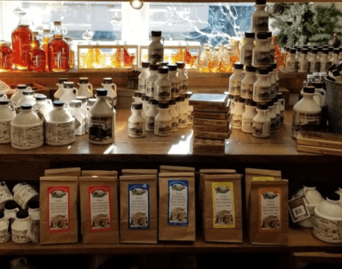 A rustic display of various bottles and bags of maple syrup and related products on wooden shelves.
