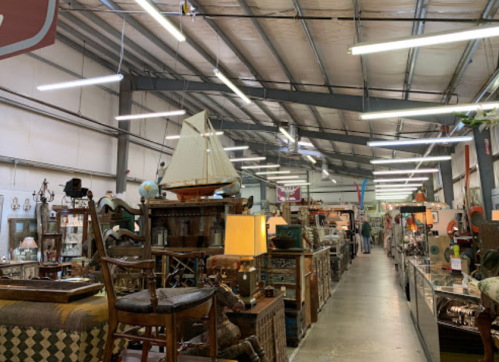 A spacious antique shop filled with various vintage items, furniture, and decor under bright overhead lights.