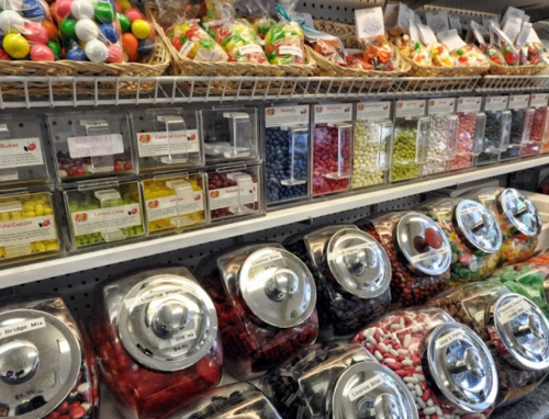 A colorful display of various candies in jars and baskets on shelves, showcasing a variety of shapes and colors.
