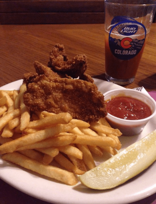 A plate of crispy fried chicken with French fries, a side of dipping sauce, and a glass of beer.