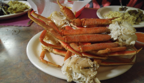 A plate piled high with cooked crab legs, accompanied by a small dish of dipping sauce.