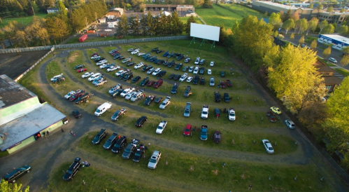 Aerial view of a drive-in movie theater with numerous parked cars and a large blank screen in the background.