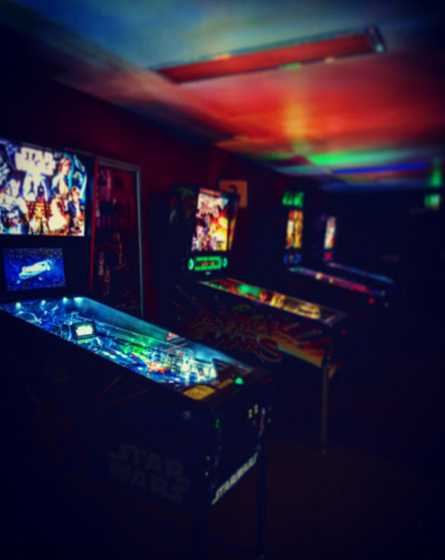 A dimly lit arcade featuring multiple Star Wars-themed pinball machines.