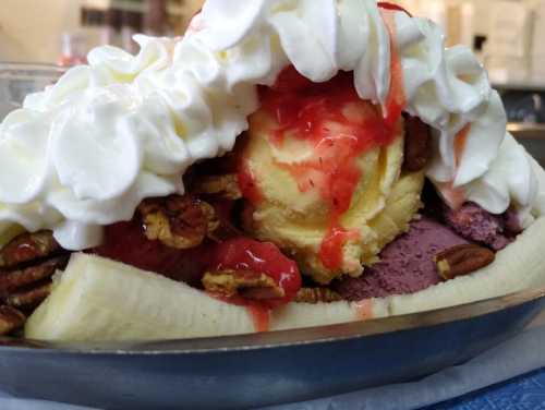 A banana split topped with whipped cream, strawberries, pecans, and scoops of vanilla and purple ice cream.
