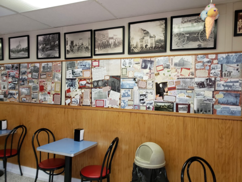A cozy café interior with blue tables, black chairs, and a wall covered in historical photos and notes.