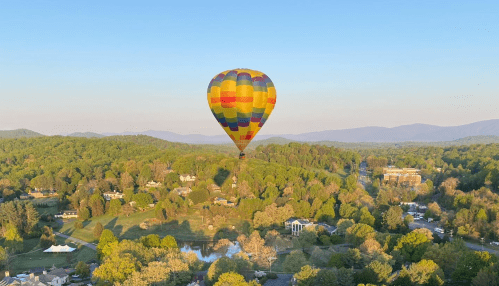 A colorful hot air balloon floats over a lush green landscape with mountains in the background and a clear blue sky.