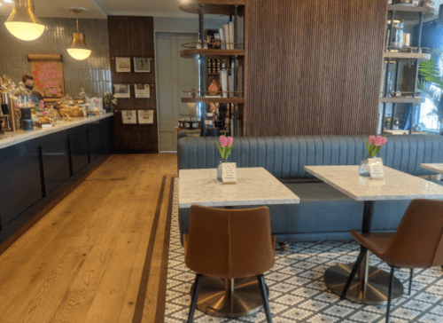 A cozy café interior with marble tables, a blue banquette, and fresh flowers, featuring a counter in the background.