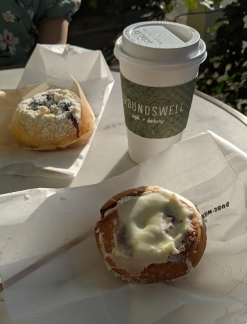 A coffee cup and two pastries on a table, with one pastry topped with icing and the other with powdered sugar.