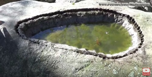 A natural stone basin filled with green water, surrounded by rough rock edges and moss.