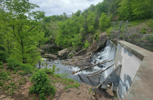 A serene landscape featuring a waterfall cascading over a dam, surrounded by lush green trees and rocky terrain.