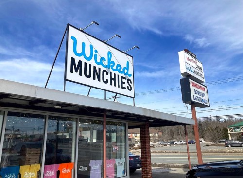 Sign for "Wicked Munchies" on a building, with colorful shirts displayed and a clear blue sky in the background.