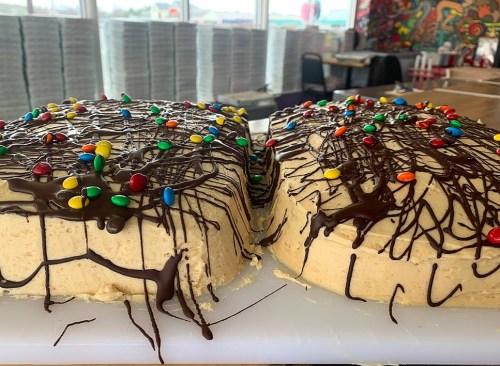 A large cake with colorful candy and chocolate drizzle, displayed in a bright, modern setting.