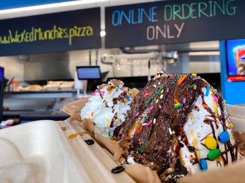 A close-up of a dessert with ice cream, chocolate sauce, and sprinkles, with a sign for online ordering in the background.