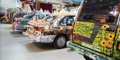 Three creatively decorated cars covered in various colorful stickers and art, displayed in a spacious indoor venue.