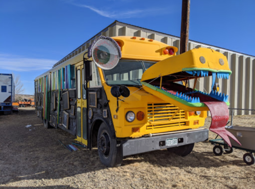 A colorful bus with a dragon head design, featuring a large open mouth and a long tongue, parked beside a building.