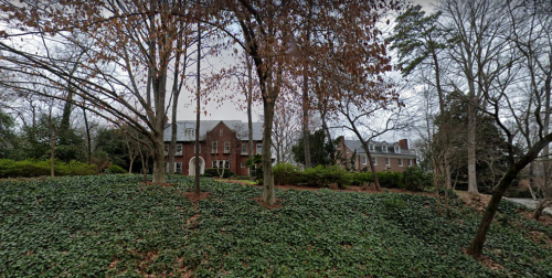 A large brick house surrounded by trees and ivy-covered ground, set in a quiet, wooded area.