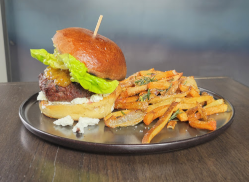 A gourmet burger with lettuce and cheese on a plate, accompanied by crispy fries.