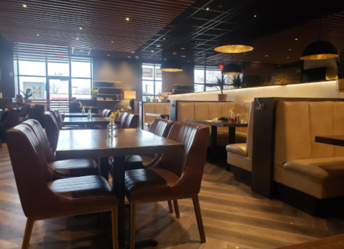 Modern restaurant interior with wooden tables, leather chairs, and soft lighting, featuring booths and a cozy atmosphere.