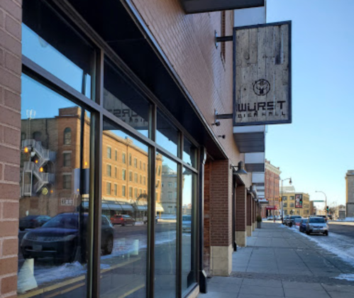 Exterior view of a building with a sign for "Wurst Beer Hall," featuring large windows and a snowy sidewalk.