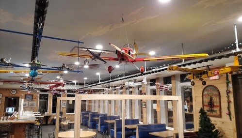 A restaurant interior featuring model airplanes hanging from the ceiling, with wooden tables and blue seating.