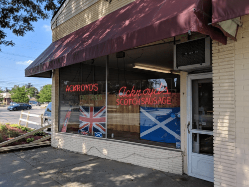 A storefront with a maroon awning, featuring neon signs for "Ackroyd's Pastries" and "Ackroyd's Scotch Sausage."