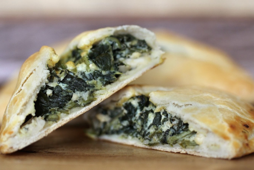 A close-up of a flaky pastry filled with spinach and cheese, cut in half to reveal the green filling.
