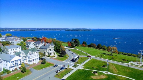 A scenic view of a coastal town with colorful trees, boats in the water, and clear blue skies.
