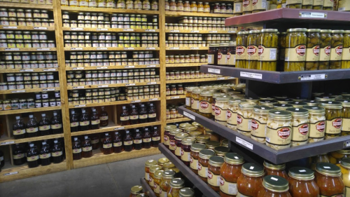 A well-stocked pantry with shelves of various jars, including pickles, sauces, and preserves.