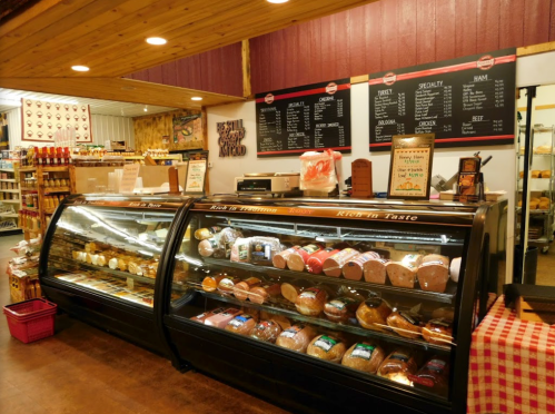 A deli display case filled with various meats and cheeses, with a menu board and rustic decor in the background.