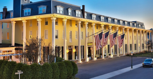 Historic yellow hotel with large columns and American flags, set against a clear evening sky.