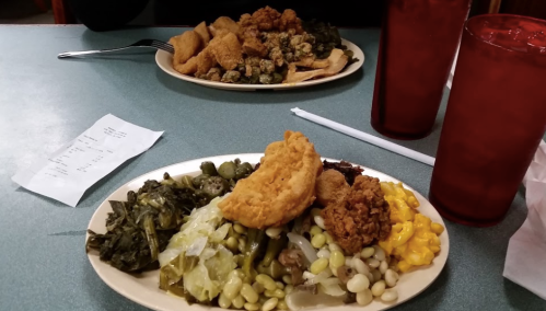 A plate of Southern food with fried chicken, greens, corn, and okra, alongside a second plate in the background.
