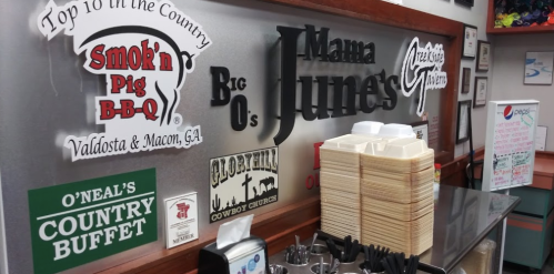 Signage featuring various restaurant names and logos, including Smokin' Pig BBQ and Mama June's, in a dining area.