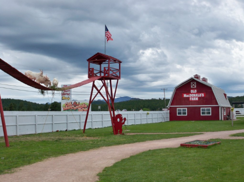 A red barn labeled "Old MacDonald's Farm" with a lookout tower and goats on a rope bridge under a cloudy sky.
