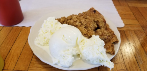 A plate with a slice of apple crisp and a scoop of vanilla ice cream on a wooden table.