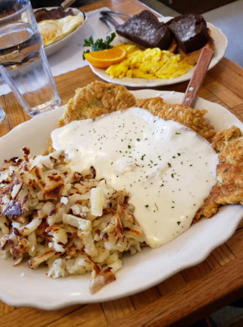 A plate of fried chicken with white gravy, served with hash browns and a side of scrambled eggs and toast.
