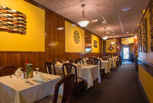 Cozy restaurant interior with yellow walls, wooden accents, and neatly set tables ready for dining.