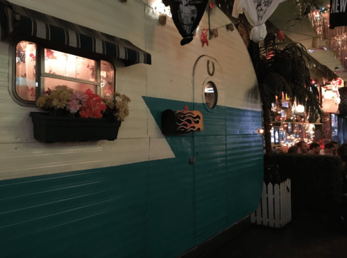 A colorful vintage trailer with a flower box and decorative mailbox, set in a lively, illuminated environment.