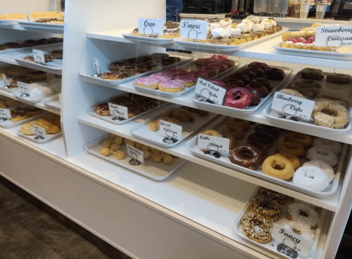 A display case filled with various donuts, including glazed, chocolate, and specialty flavors, all labeled.