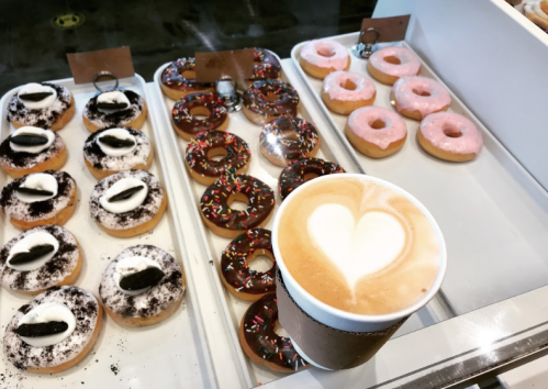 A display of assorted donuts with a latte featuring a heart-shaped foam design in the foreground.