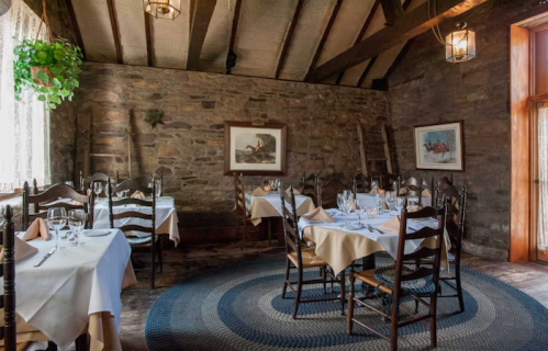 Cozy restaurant interior with wooden beams, stone walls, and elegantly set tables. Warm, inviting atmosphere.