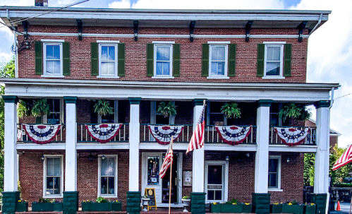Historic brick building with green shutters, decorated with red, white, and blue bunting, and American flags.