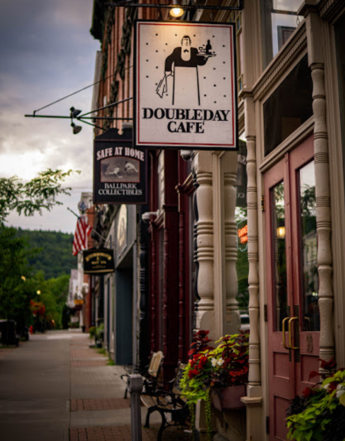 A quaint street scene featuring the Doubleday Café sign and nearby shops, with flowers and a cloudy sky.