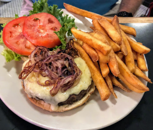 A juicy burger topped with melted cheese and fried onions, served with lettuce, tomato, and a side of golden fries.