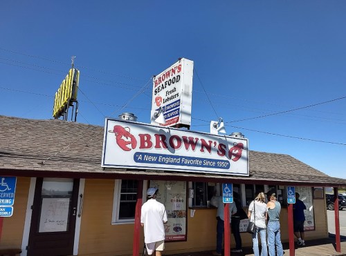 A seafood restaurant named Brown's, featuring a sign and people waiting outside under a clear blue sky.