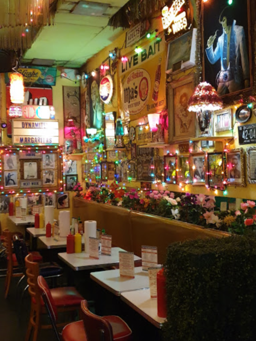 Colorful restaurant interior with vibrant decor, string lights, and framed art, featuring tables and condiment bottles.