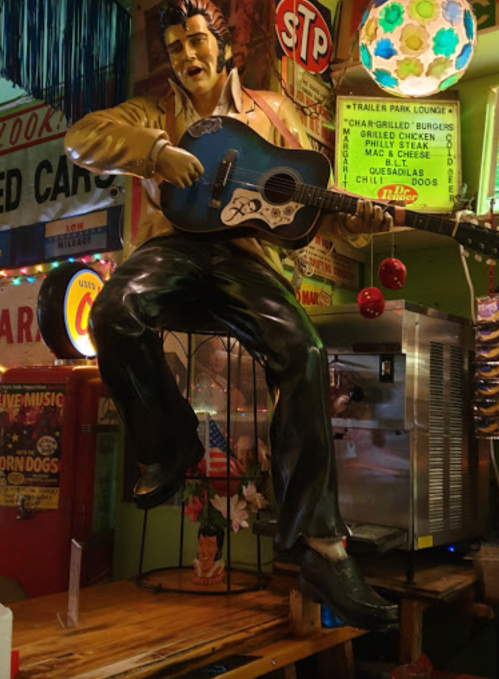 A life-sized Elvis Presley statue playing a blue guitar, surrounded by colorful retro decor in a lively diner setting.