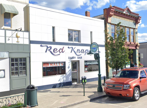 Exterior of Red Knap Dairy Bar, featuring a white facade and a red vehicle parked outside, with blue skies above.