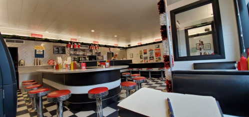 A retro diner interior with checkered floors, red stools, and a counter, decorated for the holidays.