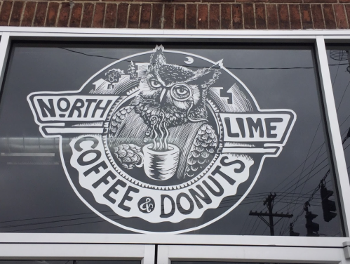 A window display featuring a stylized owl logo for "North Lime Coffee & Donuts" with a coffee cup illustration.